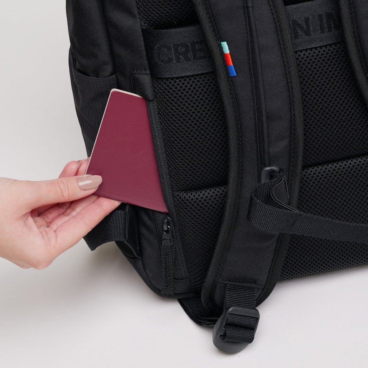 Lieblingstasche Pro Pack black backpack showing a hidden zippered back pocket with a passport being inserted.