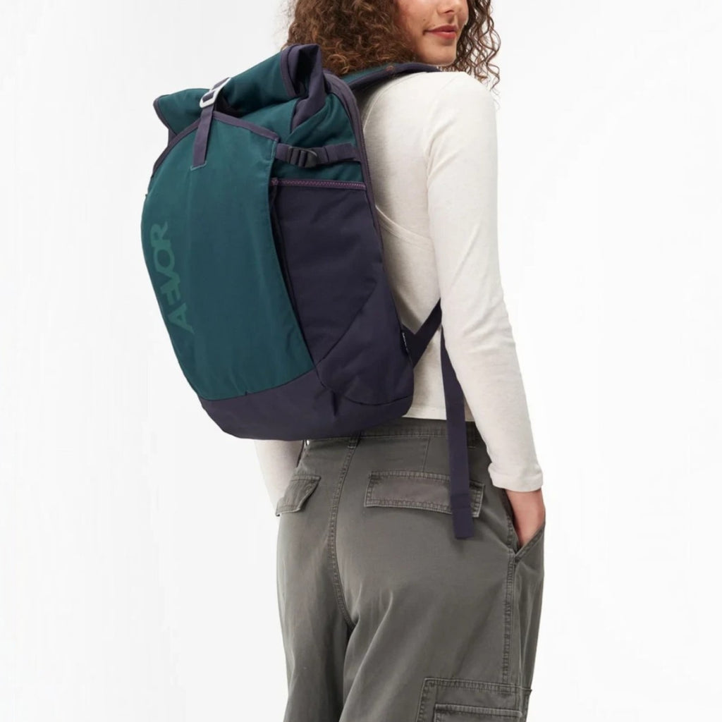 Lieblingstasche Roll Pack 2.0 in dark green and navy blue worn by a woman, featuring a rolltop and laptop compartment.