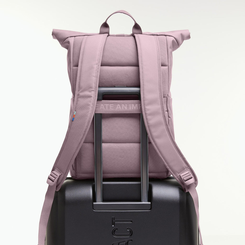 Lieblingstasche Rolltop Easy lilac backpack with padded straps, attached to a black suitcase.