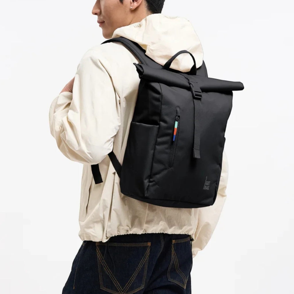 Lieblingstasche Rolltop Easy Small black backpack with rolltop closure and side pockets worn by a man.