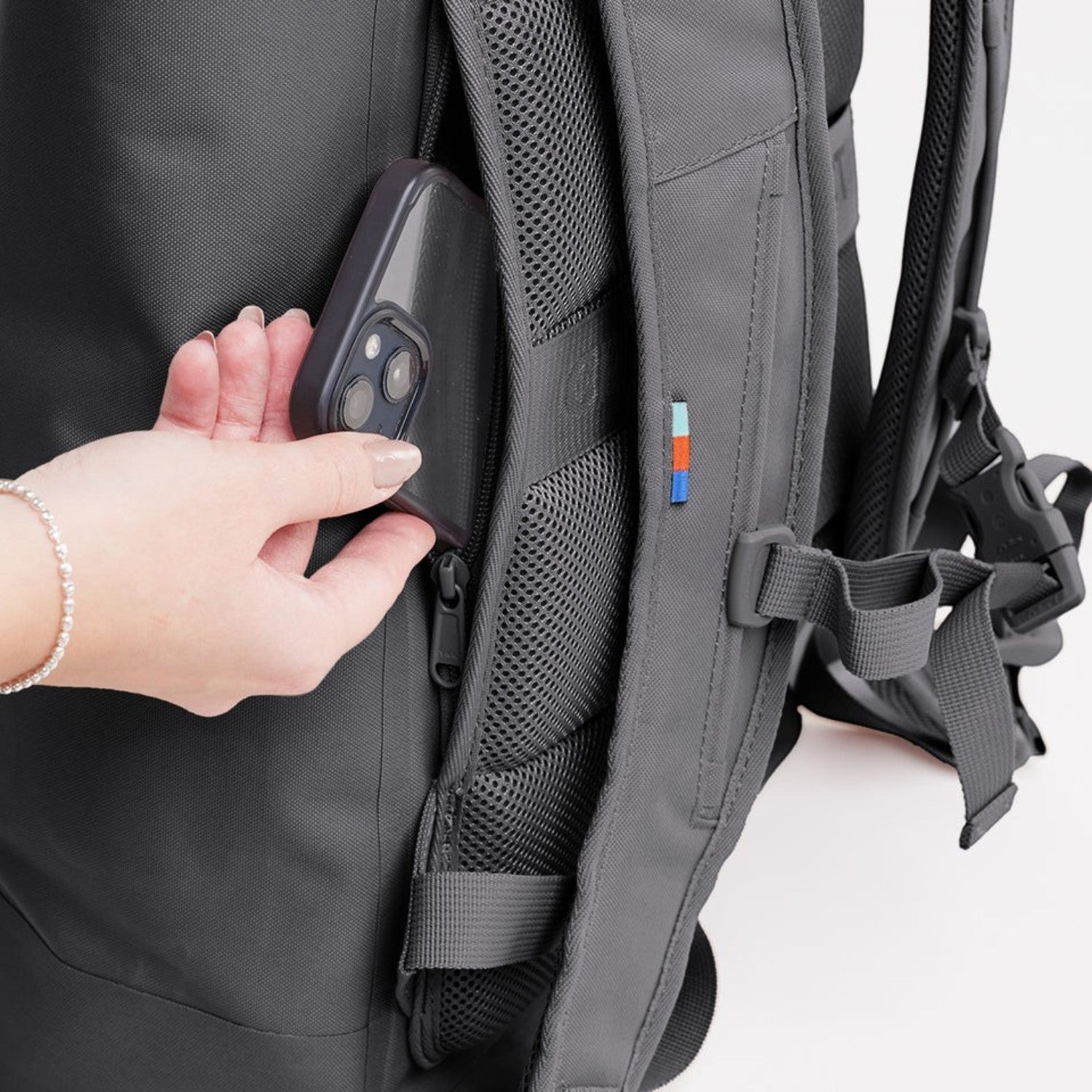 Lieblingstasche Rolltop Lite 2.0 backpack in grey showing a hand placing a smartphone into the side zipper pocket