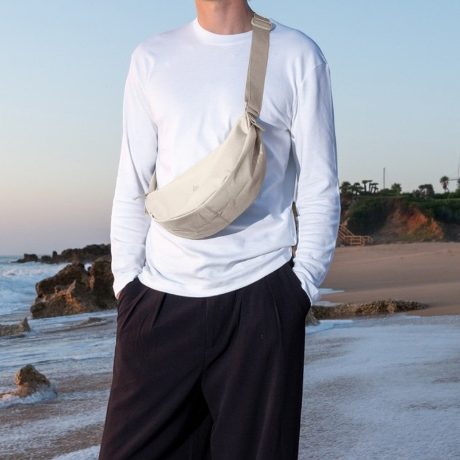 Lieblingstasche small moon bag in beige canvas with adjustable strap worn across chest by a man on a beach.