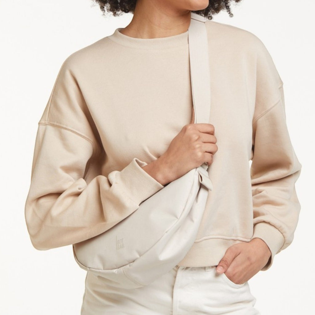 Lieblingstasche small moon bag in light beige, worn crossbody by a woman with curly hair.