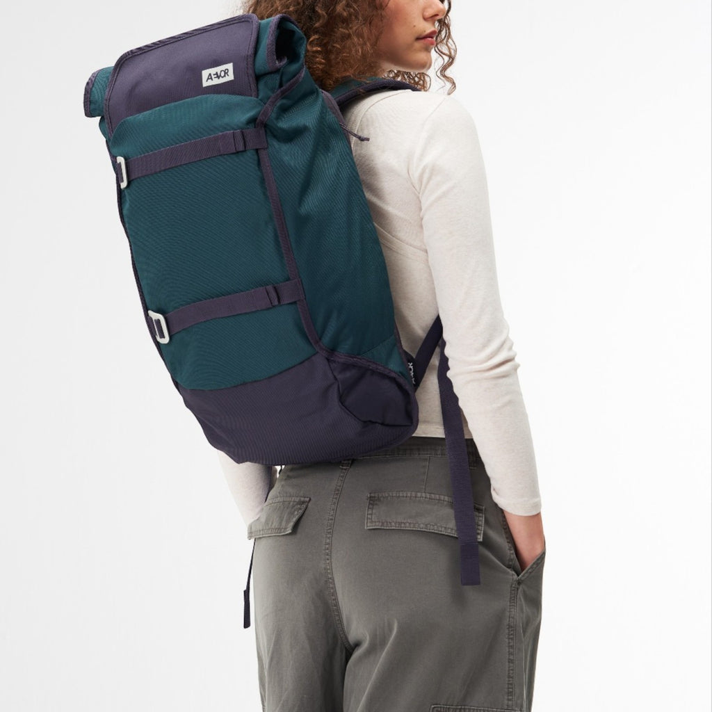 Lieblingstasche Trip Pack backpack in teal and dark purple worn by a woman against a white background